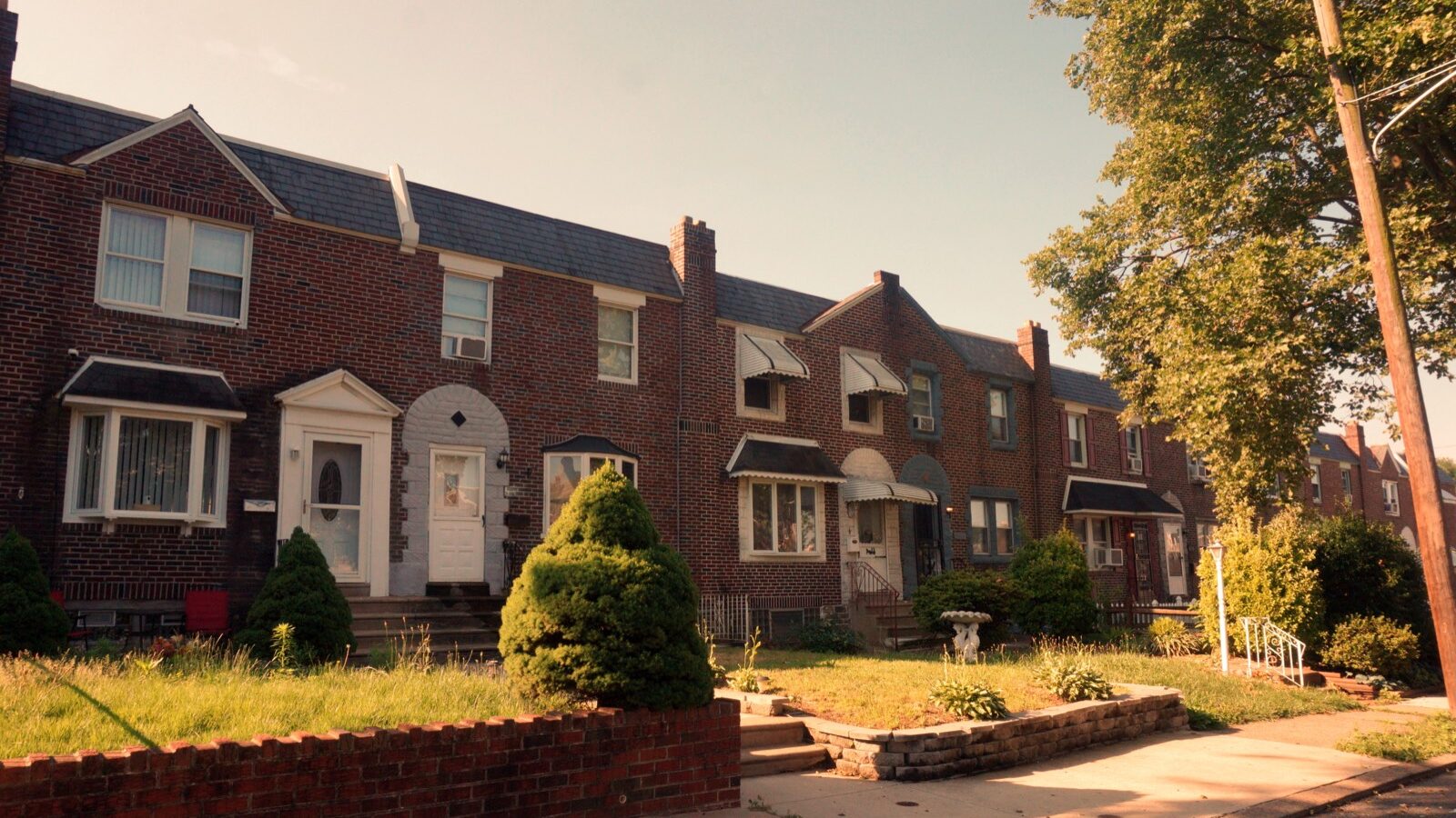 Brick row houses with small front lawns at sunrise.