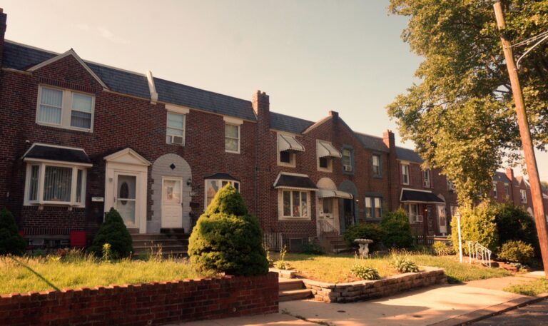 Brick row houses with small front lawns at sunrise.