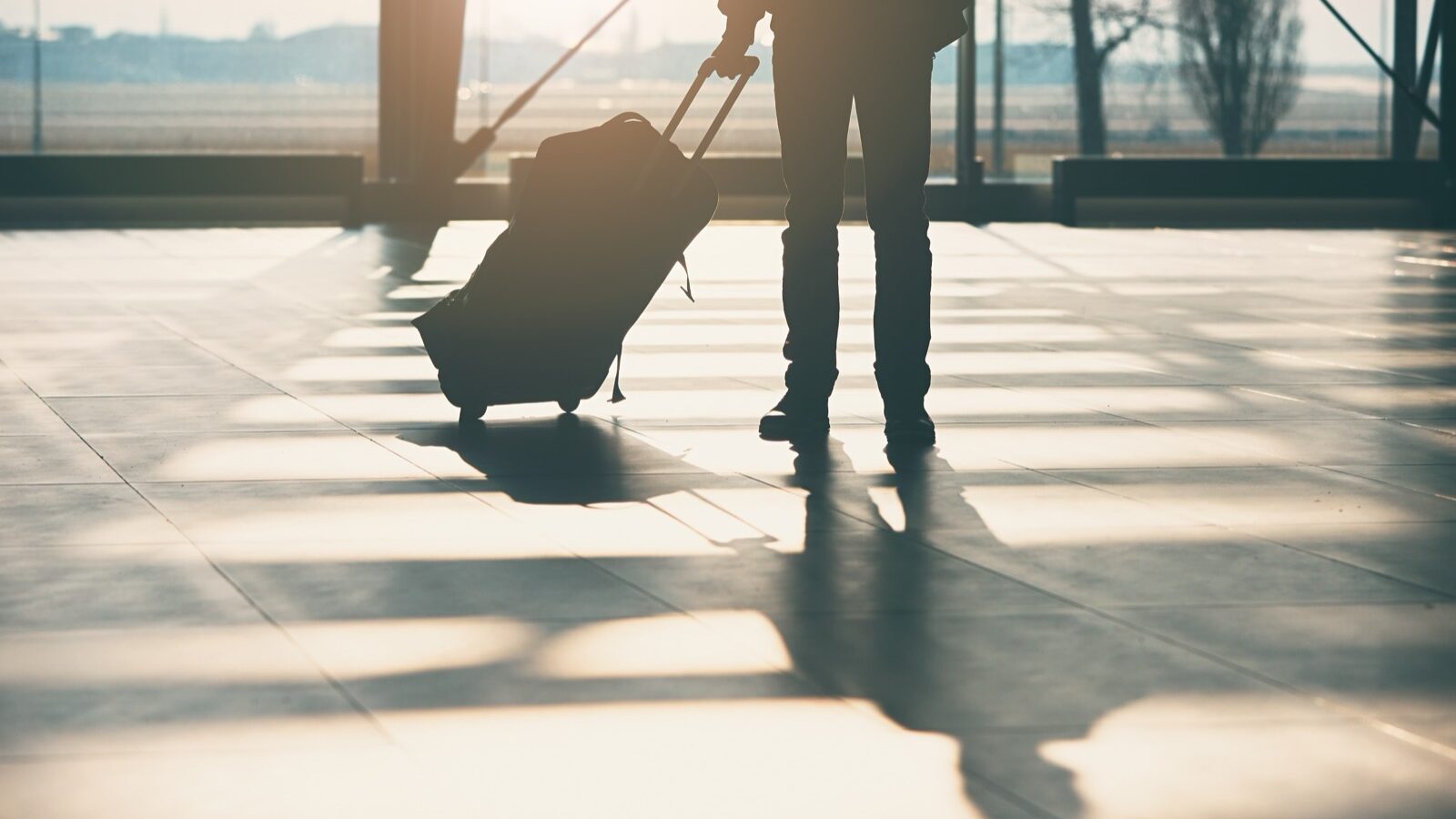 A traveler’s shadow cast across an airport terminal floor.